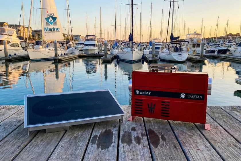 Wallas 85DT diesel hob and Wallas Spartan air heater displayed on a wooden dock with sailboats in the background marina.