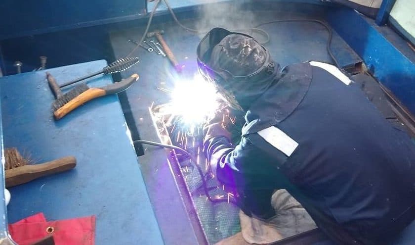 Professional marine engineer performing structural welding on a steel narrowboat deck to repair a redundant heater flue hole.